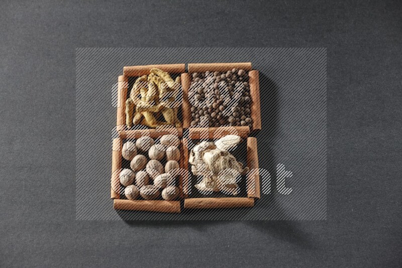 4 squares of cinnamon sticks full of turmeric fingers, allspice, dried ginger and nutmegs on black flooring