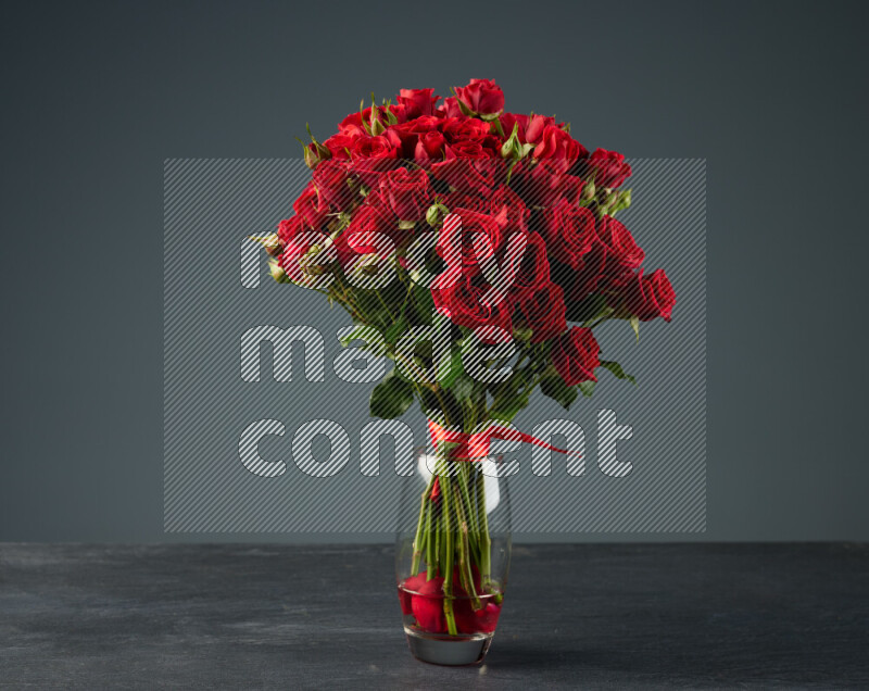 An arrangement of vivid red roses tightly bound with a red ribbon in a glass vase on black marble background