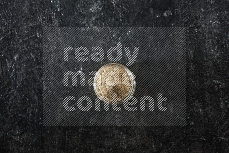 وعاء زجاجي ممتلئ ببودرة الهيل على خلفية سوداء