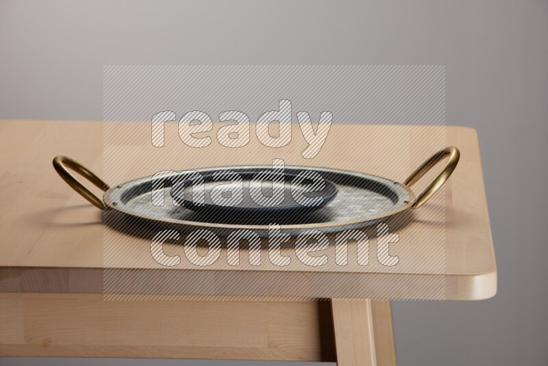 black plate placed on a rounded stainless steel metal tray with golden handels on the edge of wooden table