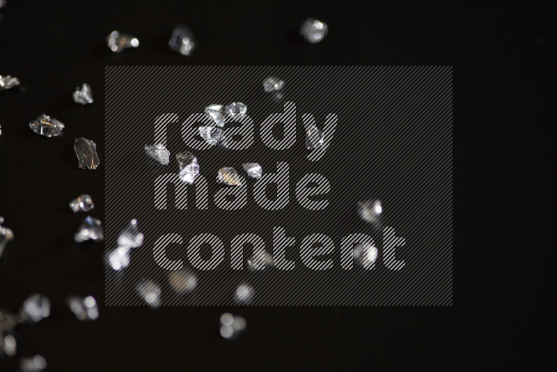 Silver shimmering fragments of glass scattered on a black background
