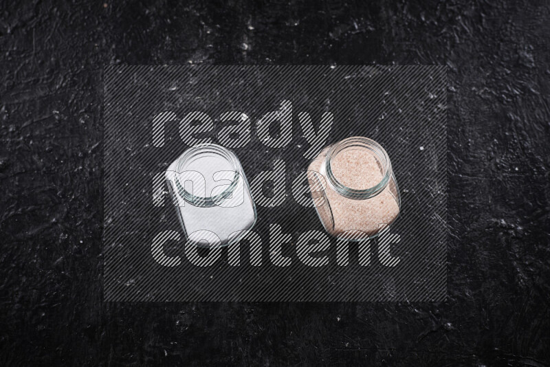 2 glass jars one is filled with fine himalayan salt and the other with table salt on black background
