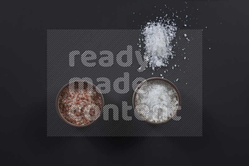 2 وعاء فخاري احدهمها ممتلئ بملح الهيمالايا والأخر بالملح الأبيض على خلفية سوداء