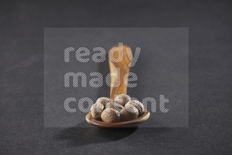 ملعقة خشبية كبيرة مليئة بحبوب جوزة الطيب الكاملة على خلفية سوداء