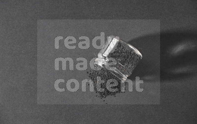 A flipped glass jar full of black seeds and the seeds spread out on a black flooring