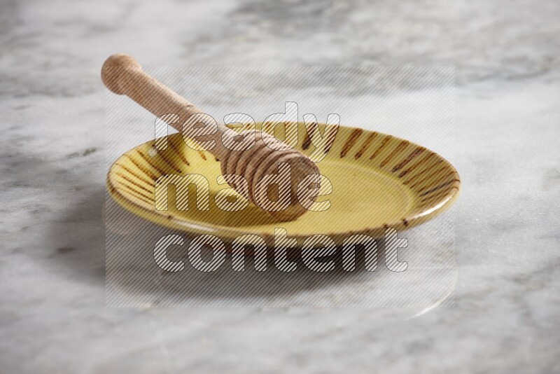 Multicolored pottery plate with wooden honey dipper in it on grey marble background