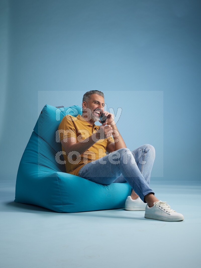 A man sitting on a blue beanbag and talking on the phone