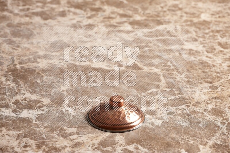 A small copper pot lid on beige marble background
