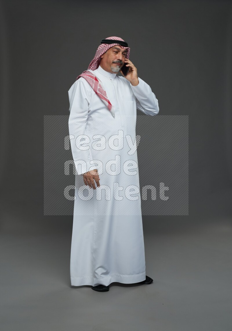 Saudi man with shomag Standing talking on phone on gray background