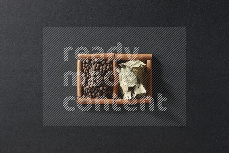 مربعان من أعواد القرفة ممتلئان ببهار الفلفل الحلو وأوراق الغار علي خلفية سوداء