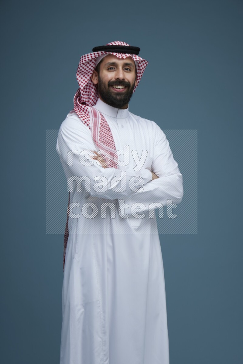 A man posing in a blue background wearing Saudi Thob and Shomag