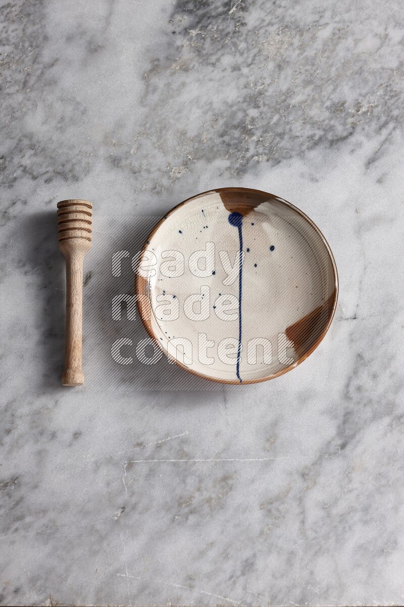 Multicolored pottery plate with wooden honey dipper on the side on grey marble background