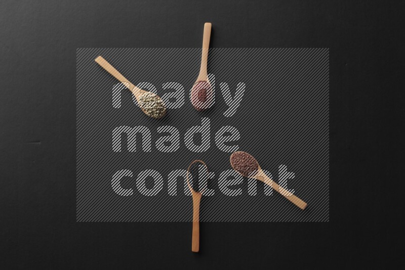 wooden spoons filled with white peppers, mustard seeds, black seeds, garden cress, cumin and flax on black flooring