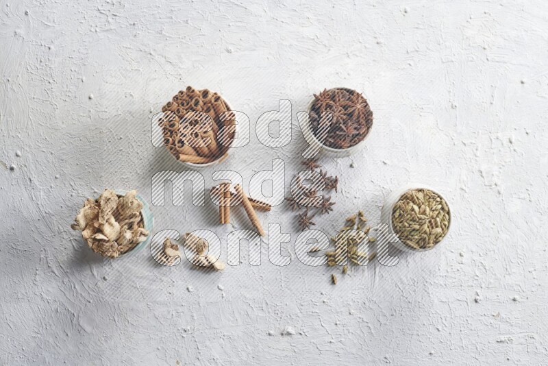 Cardamom, ginger, cinnamon sticks and star anise in 4 bowls on a textured white background