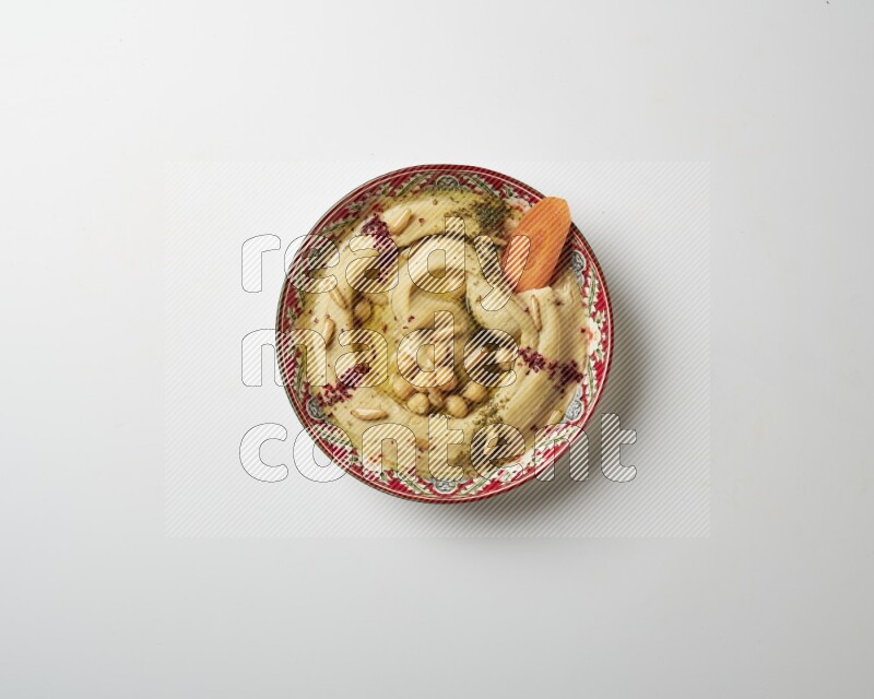 Hummus in a red plate with patterns garnished with zaatar & sumak on a white background