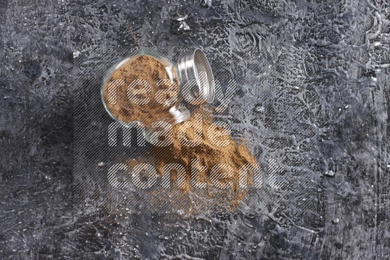 Flipped herbal glass jar full of cinnamon powder on textured black background