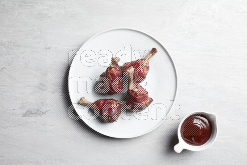drumstick wrapped in bacon on round white ceramic plate on grey textured countertop