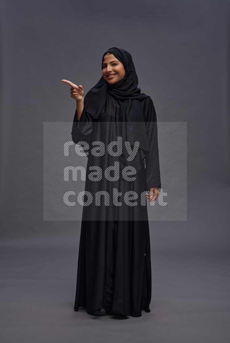 Saudi woman wearing Abaya standing interacting with the camera on gray background