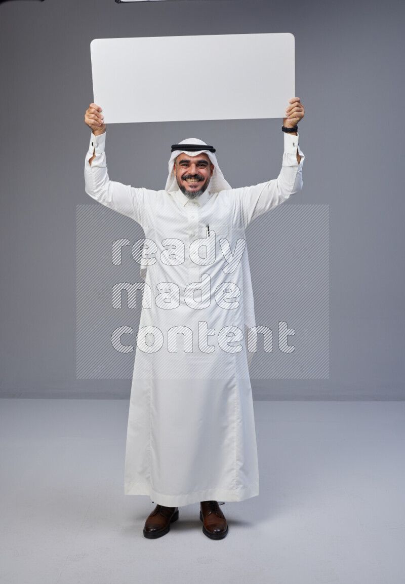 Saudi man Wearing Thob and white Shomag standing holding board on Gray background