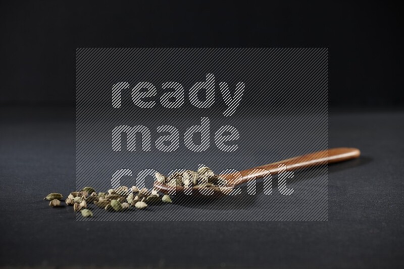 A wooden ladle full of cardamom on black flooring