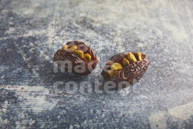 two pistachios stuffed madjoul dates on a rustic blue background