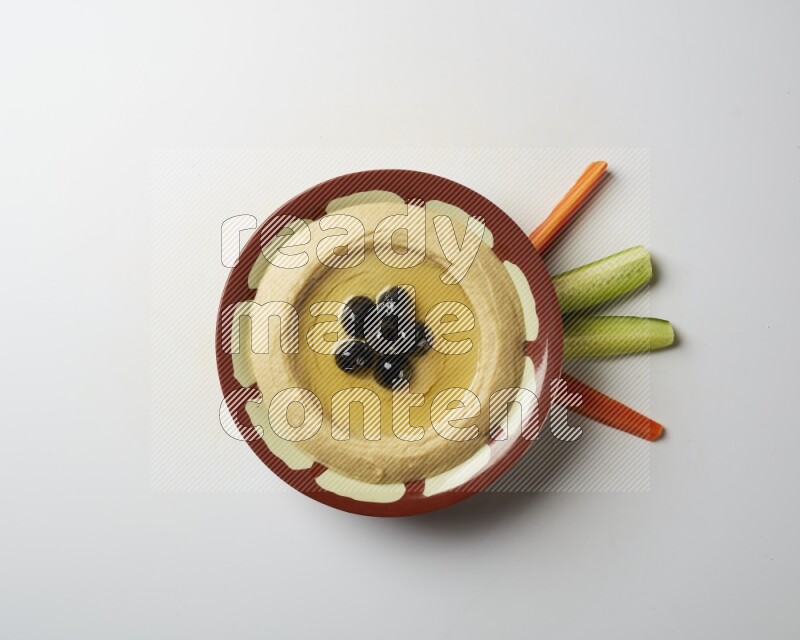 Hummus in a traditional plate garnished with black olives on a white background