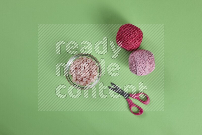 A pink collection of sewing and tailoring tools arranged on a green background