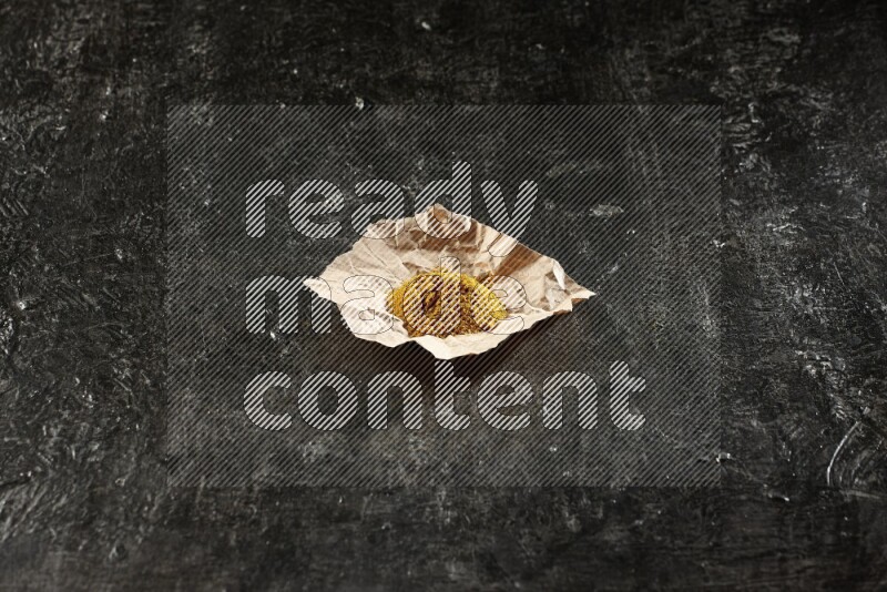 Turmeric powder in a crumpled piece of paper on textured black flooring