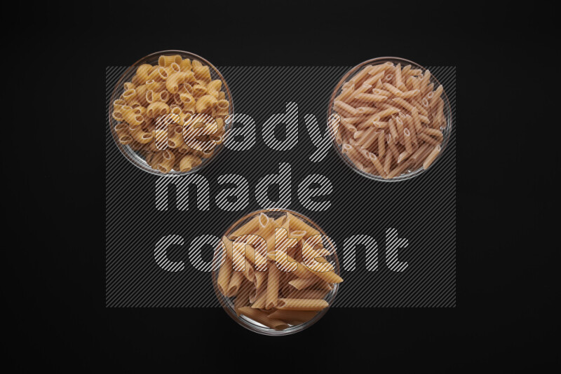 Different pasta types in glass bowls on black background