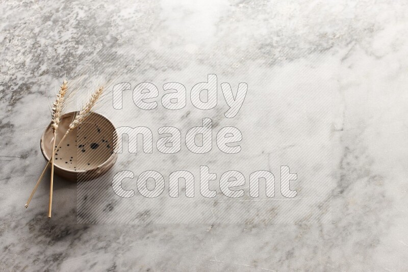 Wheat stalks on multicolored pottery bowl on grey marble background