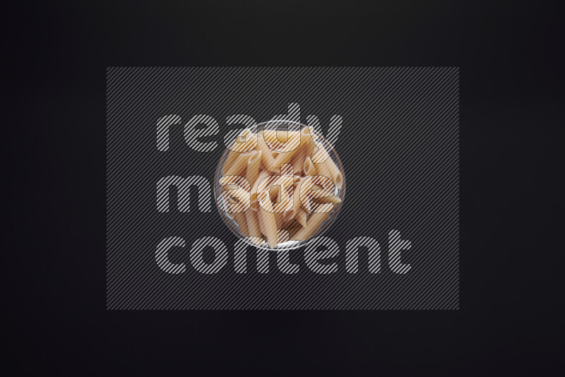 Penne pasta in a glass bowl on black background