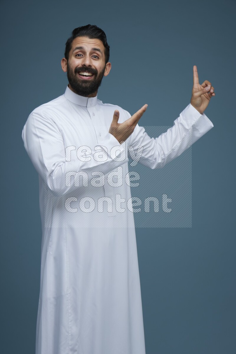 A man pointing in a blue background wearing Saudi Thob