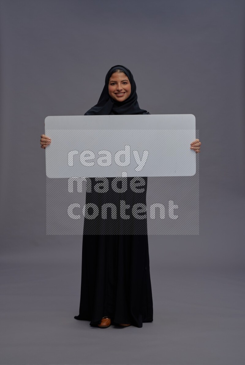 Saudi woman wearing Abaya standing holding white board on gray background