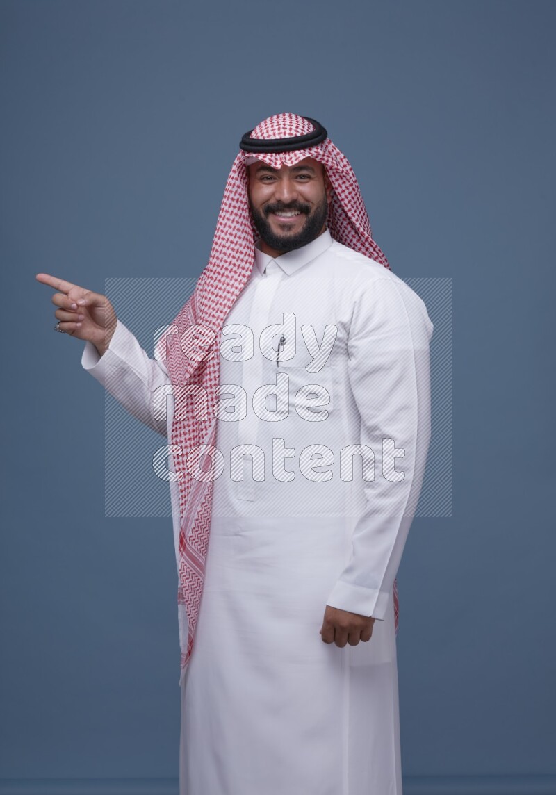 A Saudi man posing on blue background wearing Thob and Shomag