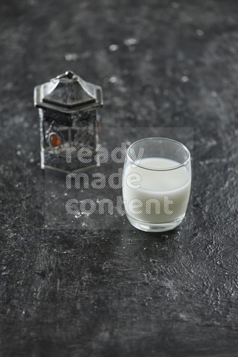 A silver lantern with different drinks, dates, nuts, prayer beads and quran on textured black background