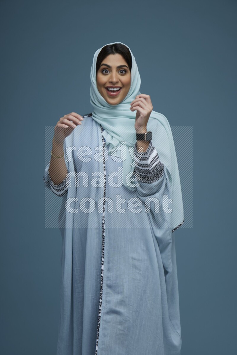 A woman posing in a blue background wearing a blue Abaya with hijab