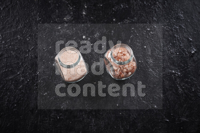 2 glass jars one is filled with fine himalayan salt and the other with coarse himalayan salt on black background