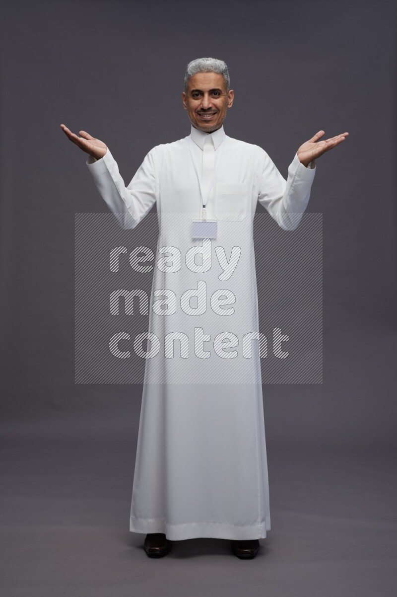 Saudi man wearing thob with neck strap employee badge standing interacting with the camera on gray background