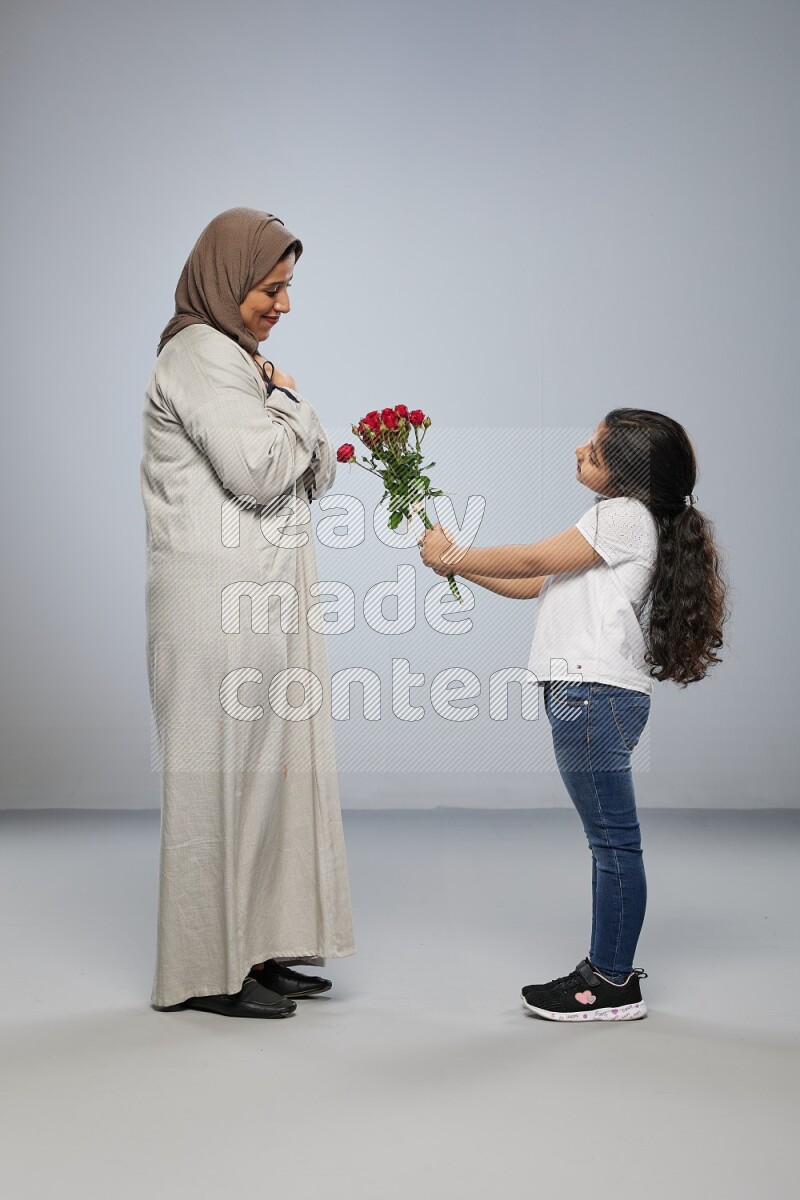 A girl standing giving flowers to her mother on gray background
