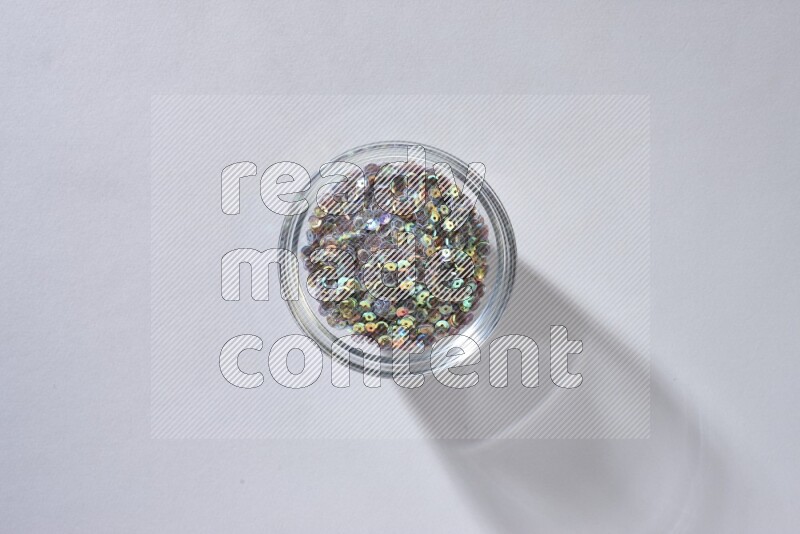 Colored flat sequins in a glass bowl on grey background