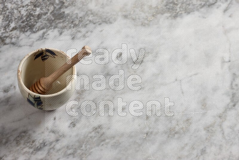 Decorative pottery bowl with wooden honey dipper in it on grey marble background