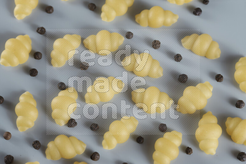 Raw pasta with different ingredients such as cherry tomatoes, garlic, onions, red chilis, black pepper, white pepper, bay laurel leaves, rosemary, cardamom and mushrooms on light blue background