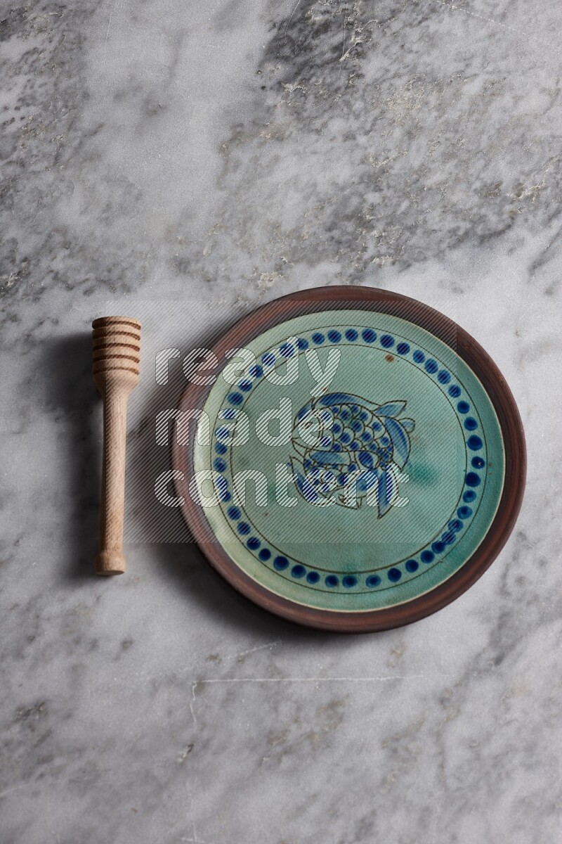 Decorative pottery plate with wooden honey dipper on the side on grey marble background