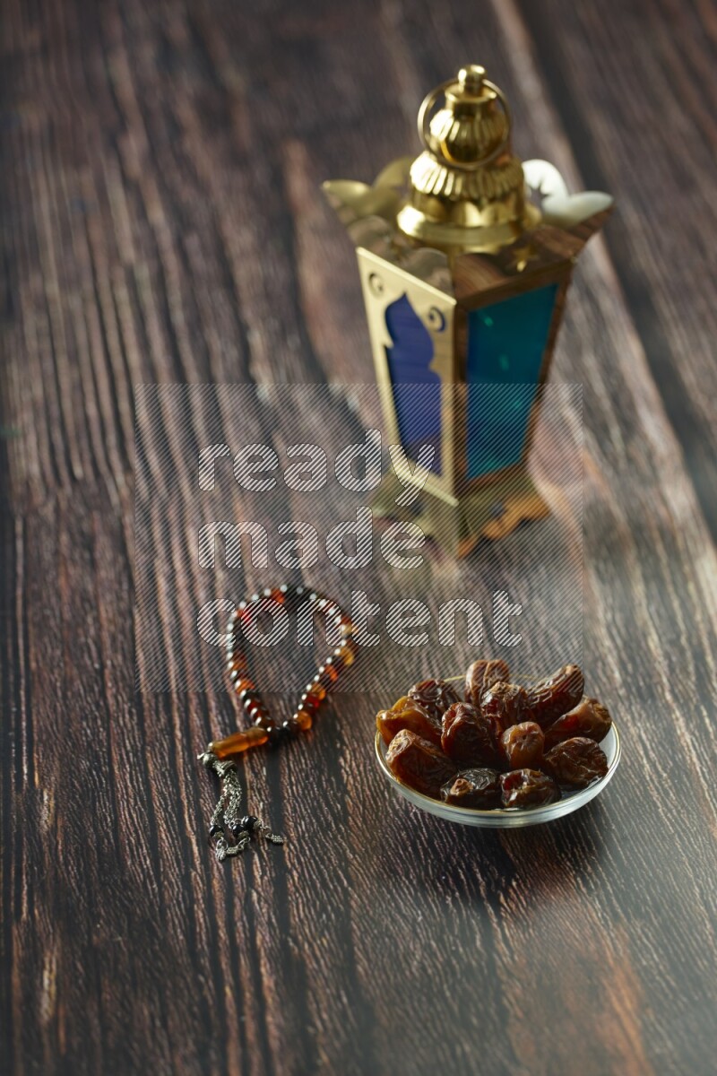 A golden lantern with different drinks, dates, nuts, prayer beads and quran on brown wooden background