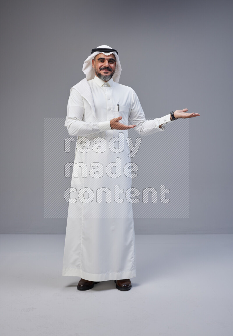 Saudi man Wearing Thob and white Shomag standing interacting with the camera on Gray background