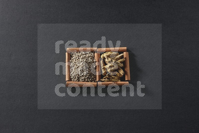 مربعان من أعواد القرفة ممتلئان بحبوب الفلفل الأبيض وأصابع الكركم علي خلفية سوداء