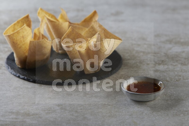 wonton cups with soy sauce ramkin on circle slate on grey textured counter top