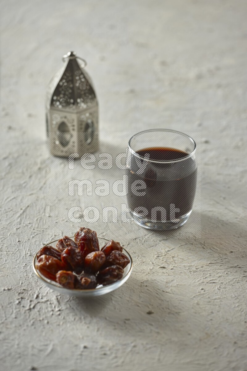 A silver lantern with different drinks, dates, nuts, prayer beads and quran on textured white background