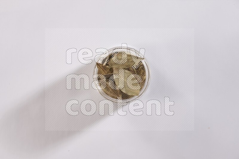 A glass jar filled with dried bay leaves on white flooring