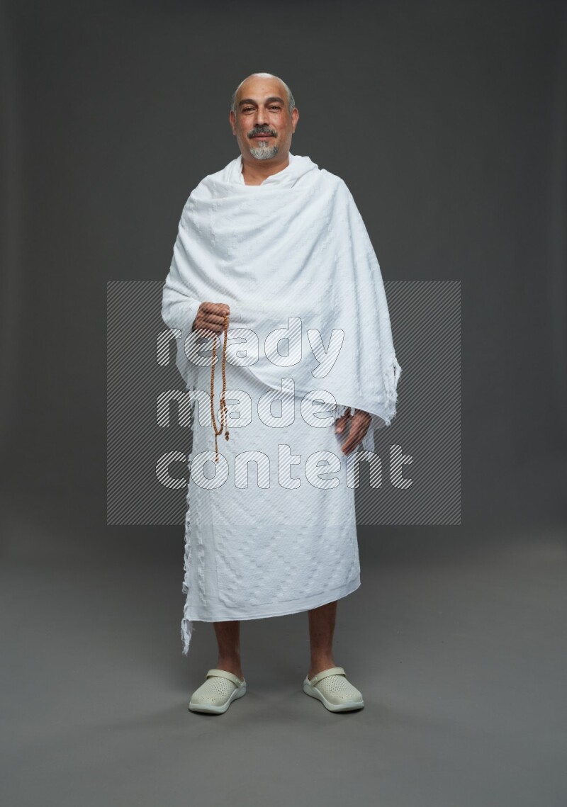 A man wearing Ehram Standing holding rosary on gray background